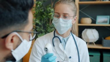 Dost canlısı doktor, evdeki hasta adamla konuşuyor. Vücut sıcaklığını ölçüyor ve termometreye dokunmuyor.