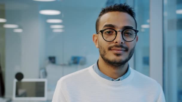 Retrato del joven hombre de Oriente Medio en gafas mirando a la cámara con cara seria en la oficina — Vídeos de Stock