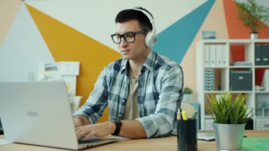 Ofis çalışanı iş yerindeki kulaklıklarda dizüstü bilgisayar kullanıyor ve müzik dinliyor.