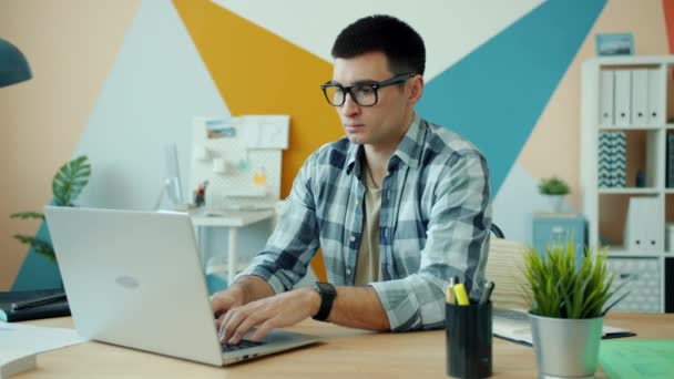 Tired young man using laptop in office then touching head feeling exhausted — Stock Video