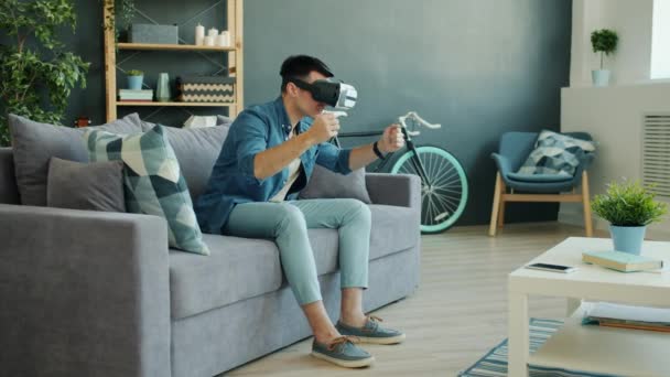 VR gözlüklü neşeli adam yavaş hareket ediyor. Evde araba kullanmaktan zevk alıyor. — Stok video