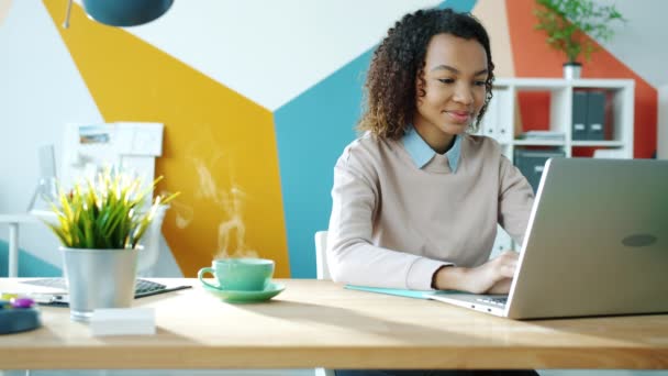 Cinemagraph loop de bela menina afro-americana usando laptop no escritório com bebida quente na mesa — Vídeo de Stock