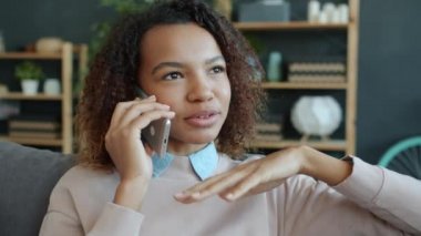 Cep telefonuyla konuşan ve evinde gülümseyen mutlu Afrikalı Amerikalı kadının yavaş çekimleri.