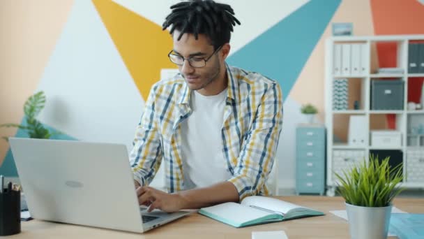 Az afro-amerikai srác lassú mozgása modern laptoppal az irodában egyedül dolgozik — Stock videók