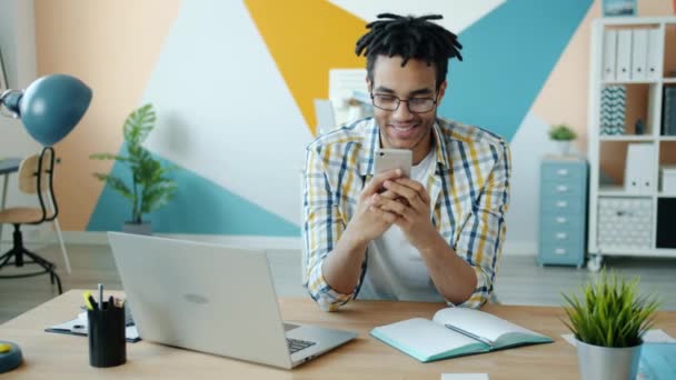 Mouvement lent de l'homme afro-américain joyeux appréciant les activités smartphone sur le lieu de travail — Video