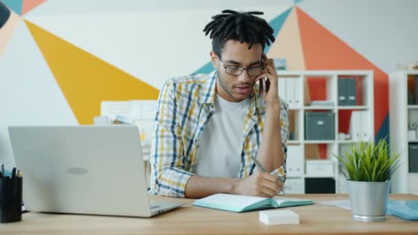 혼성 인종 남자 사무실에서 노트북으로 글을 쓰고 웃으면서 휴대 전화로 말하는 모습 — 비디오
