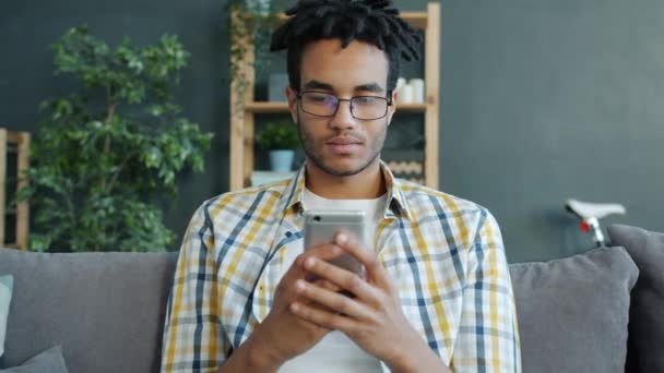 Šťastný africký americký student pomocí smartphone doma relaxaci na pohovce sám — Stock video