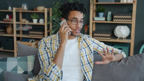 Powolny ruch uśmiechniętego afro-amerykanina mówiącego przez telefon komórkowy w mieszkaniu — Wideo stockowe