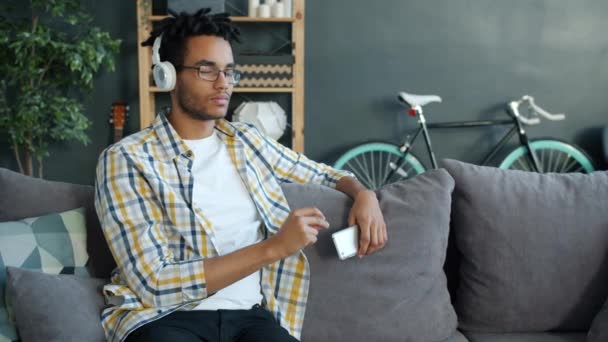 Mouvement lent de beau mixte homme appréciant la musique à travers des écouteurs tenant smartphone — Video