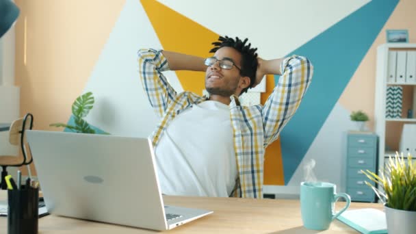 Agréable homme afro-américain assis au bureau se détendre avec une boisson chaude sur la table — Video