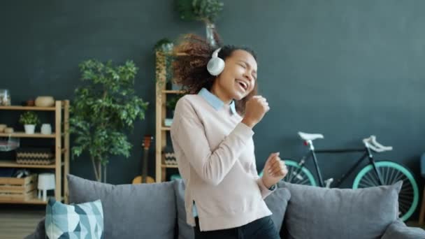 Glada afro-amerikanska tonåring dansar och sjunger hemma i hörlurar — Stockvideo