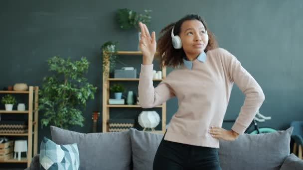 Feliz estudiante afroamericana chica bonita bailando y cantando en casa con auriculares — Vídeo de stock