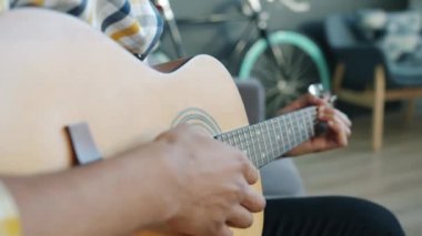 Evde gitar çalan erkek ellerinin yakın çekimi. Elinde müzik aleti var.