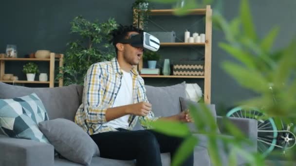 Emocionado hombre afroamericano disfrutando de gafas de realidad virtual con auriculares en casa — Vídeo de stock