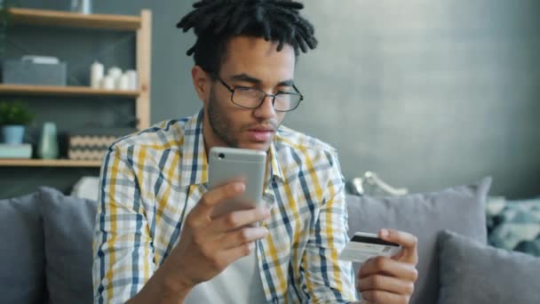 Afro-Amerikaanse man doet online betaling met bankkaart aanraken smartphone scherm binnen — Stockvideo