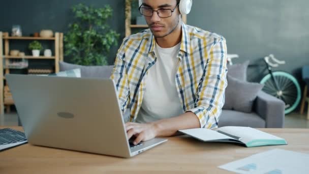 Afro-Amerikaanse student met koptelefoon die thuis met laptop typt — Stockvideo