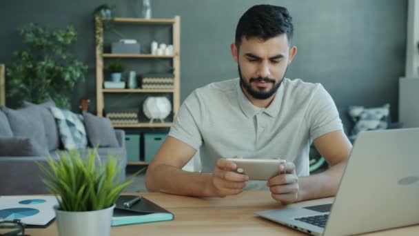 Happy Moddle Eastern man playing video game at home using modern smartphone — Stock Video