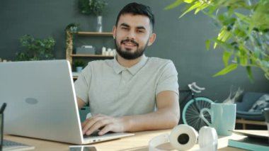 Evde dizüstü bilgisayarla çalışan neşeli, serbest çalışan genç bir gencin görüntü döngüsü portresi.