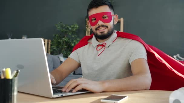 Slow motion porträtt av Mellanösterns man i superman cape och mask vid datorn skrivbord hemma — Stockvideo