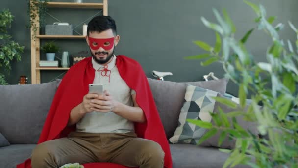 Ung man i superman kostym mask och cape med hjälp av smartphone hemma — Stockvideo