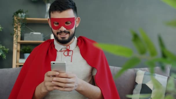 Uomo eccitato in mantello rosso e maschera utilizzando smartphone godendo di buone notizie online — Video Stock