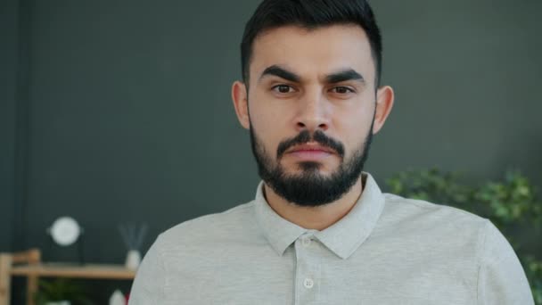 Porträtt av arabiska mannen står inomhus med allvarligt ansikte sedan ler tittar på kameran — Stockvideo