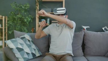 Sanal gerçeklik gözlüklü genç adamın portresi evde eğlenirken kollarını hareket ettiriyor.