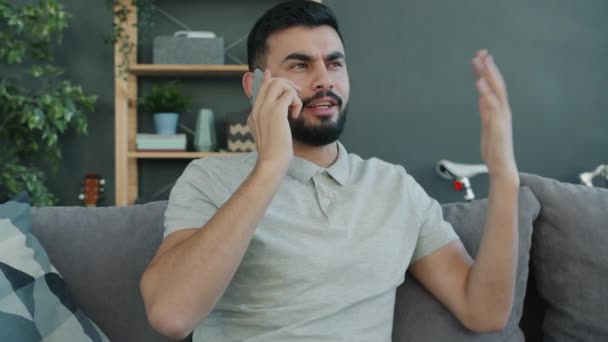 Vidám arab srác beszél mobiltelefonon gesztikulálva érzelmek megosztása otthon — Stock videók