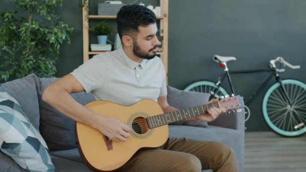 Kreativer Mann aus dem Nahen Osten spielt zu Hause Gitarre und genießt Musikinstrument — Stockvideo