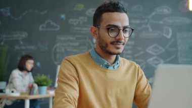 Mutlu ofis çalışanı Arap işyerinde gülerek dizüstü bilgisayar kullanıyor.