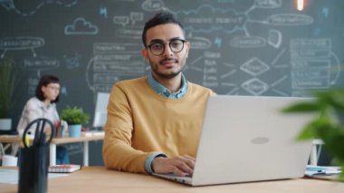 Masasında dizüstü bilgisayarı olan Afro-Amerikan bir ofis çalışanının yavaş çekim portresi.