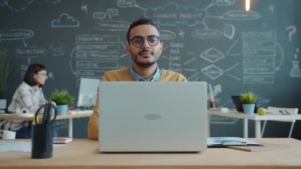 Retrato del joven trabajador de oficina árabe guapo sentado en el lugar de trabajo con el ordenador portátil — Vídeo de stock