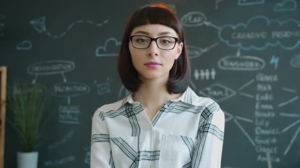 Portret poważnej młodej kobiety stojącej w biurze z tablicą w tle — Wideo stockowe