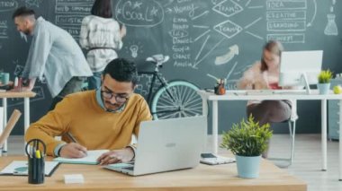 Dizüstü bilgisayar kullanan ve açık uzay ofisinde yazan melez genç adamın zaman aşımı