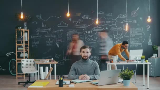 Time lapse porträtt av mannen sitter vid skrivbordet i öppna utrymme kontor medan människor kollegor arbetar — Stockvideo