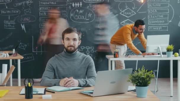 Time lapse portret van bebaarde man zitten aan het bureau en kijken naar de camera in coworking ruimte — Stockvideo