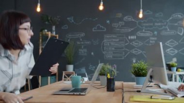 Diz üstü bilgisayar kullanan kadın ofis çalışanı iş yerindeki Arap erkek arkadaşla konuşuyor.