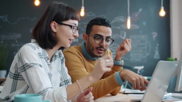Девушка и парень смешанной расы бизнес-команда говорить с помощью ноутбука в общем офисе — стоковое видео