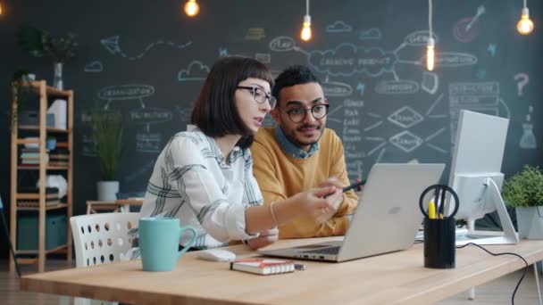 Gelukkige collega 's praten over high-five en lachen achter een bureau op de werkplek — Stockvideo