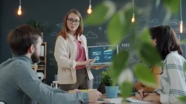 Kadın ofis çalışanı laptopun çok ırklı grupla konuştuğunu gösteren bir rapor hazırlıyor.