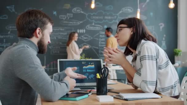 Erkek ve kadın bilgisayar ekranına bakarken iş arkadaşlarının tahtaya asılmasını tartışıyor. — Stok video