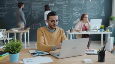 Bilgisayarla çalışan Afro-Amerikalı iş adamı sonra da ortak ofiste cep telefonuyla konuşuyor.