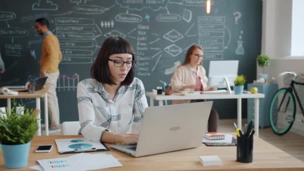 Unternehmerin benutzt Laptop im gemeinsamen Büro, während Mitarbeiter im Hintergrund beschäftigt sind — Stockvideo