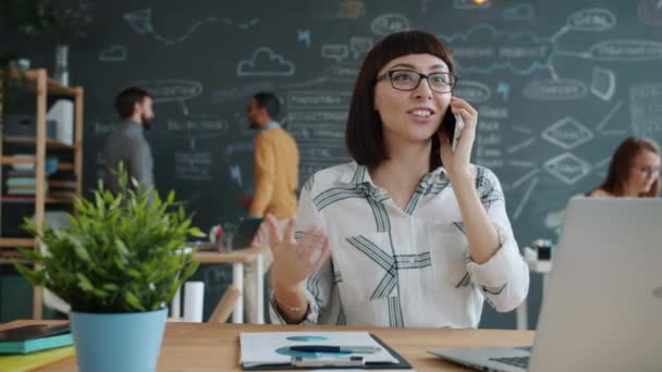 Glada flicka anställd talar på mobiltelefon på kontoret tittar på bärbar skärm — Stockvideo