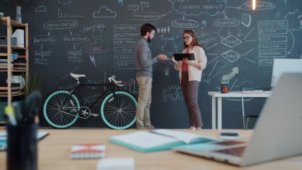 Mitarbeiter diskutieren Geschäftsidee, die in der Nähe von Tafelwand im gemeinsamen Büro steht — Stockvideo