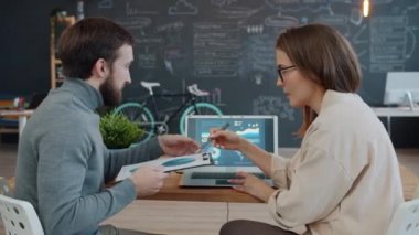 Erkek ve kadın, modern ofiste laptop ekranına bakarak iş konuşuyorlar.