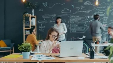 Çevrede dizüstü bilgisayar ve akıllı telefon kullanan insanlarla birlikte çalışan genç bir kadının zamanaşımına yakınlaşması