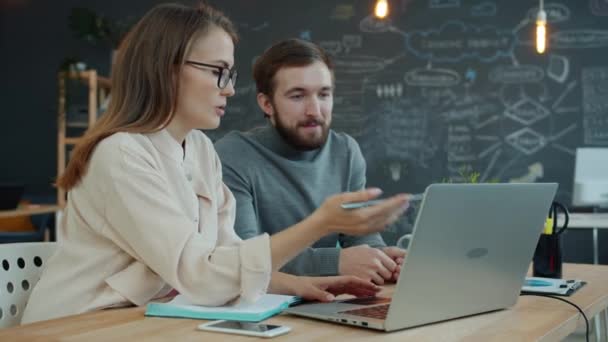 Erkek ve bayan meslektaşlar iş yerlerindeki bilgisayar ekranlarına bakarak iş konuşuyorlar — Stok video