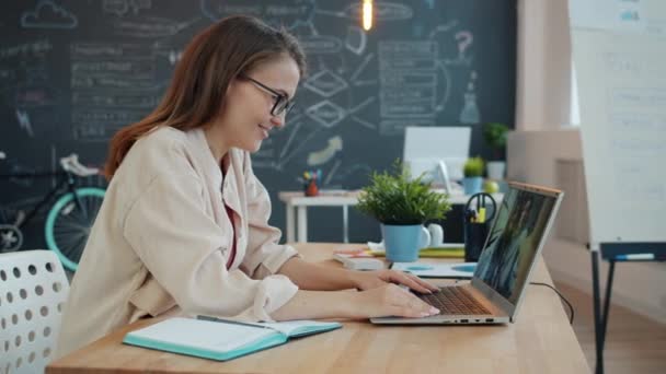 Gelukkig jonge vrouw praten vrienden online met laptop het maken van internet video gesprek zwaaien hand zitten aan bureau in office — Stockvideo