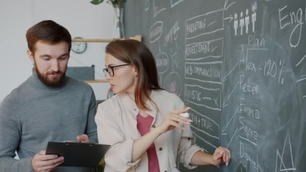 Hombre y mujer escribiendo información de negocios en pizarra en la oficina hablando de compartir ideas — Vídeos de Stock